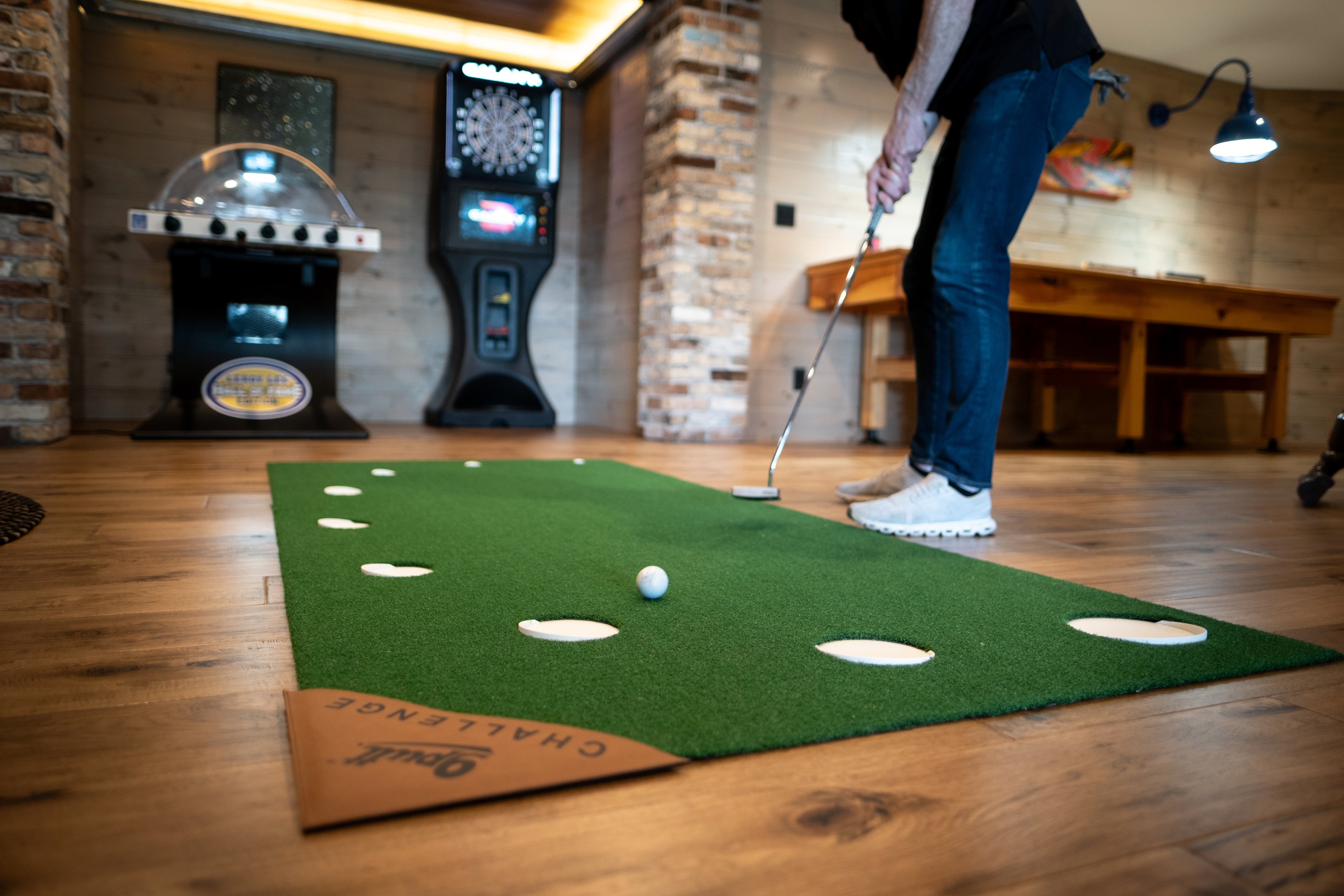 Person practicing golf swings on a simulator mat in a room with arcade games.